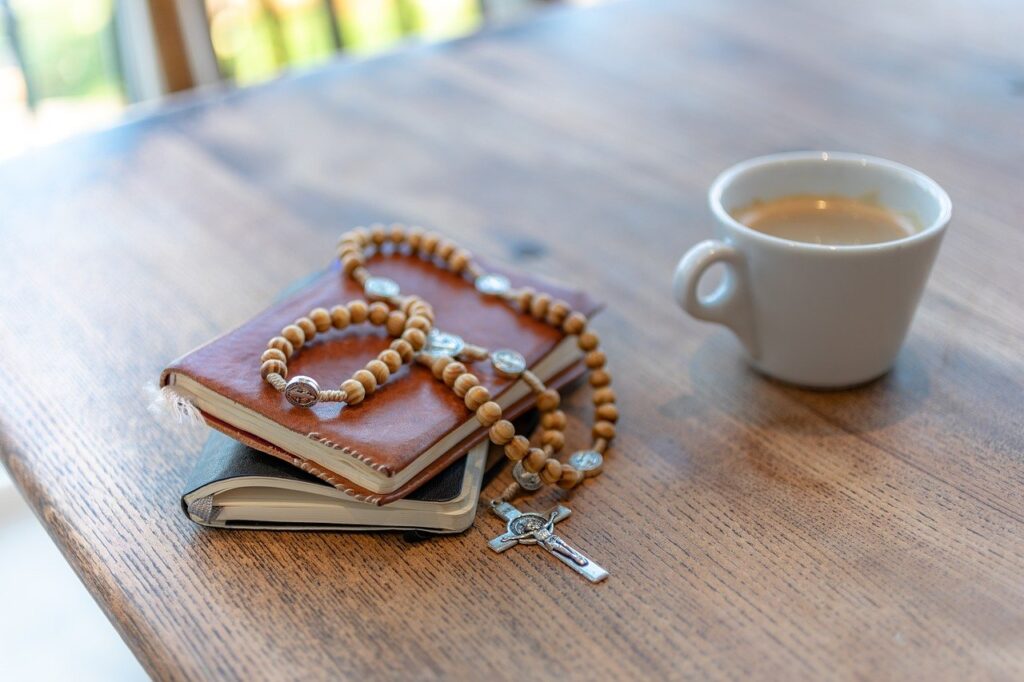 Wooden rosary and notebooks on a wooden table with a cup of coffee